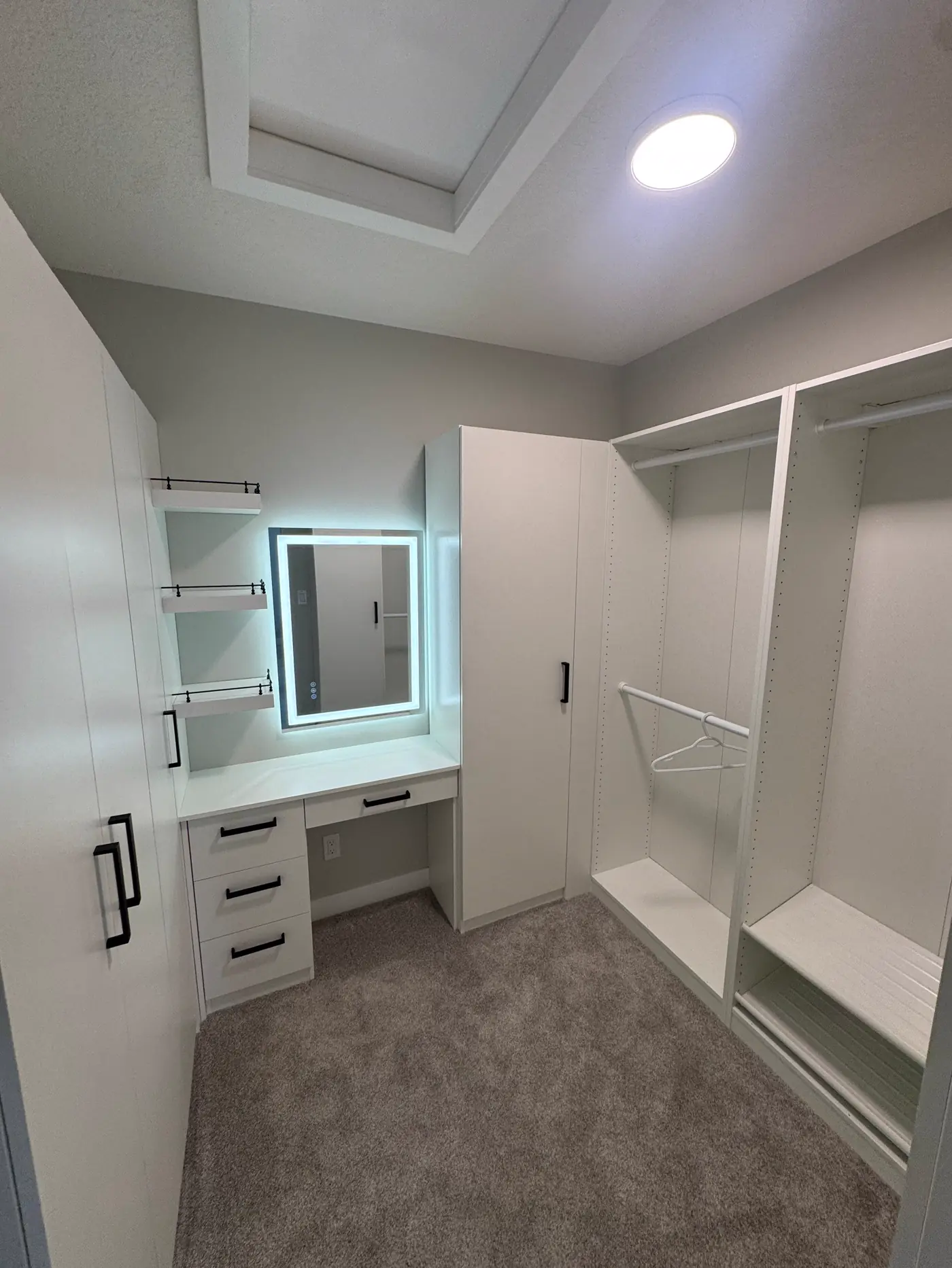 Completed custom walk-in closet with built-in cabinetry, makeup desk and illuminated mirror.